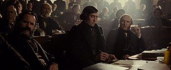 Movie still from “Lincoln” (2012), directed by Steven Spielberg – A man sitting at a table in front of a group of people; Medium shot, Over the shoulder angle