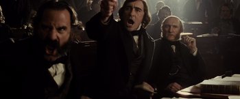 Movie still from “Lincoln” (2012), directed by Steven Spielberg – A man in a black coat is yelling at a crowd of onlookers; Medium shot, Over the shoulder angle