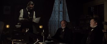 Movie still from “Lincoln” (2012), directed by Steven Spielberg – An older man sitting at a table in a dimly - lit room; Medium shot, Over the shoulder angle