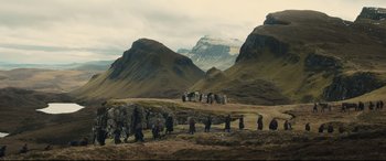 Movie still from “Macbeth” (2015), directed by Justin Kurzel – A group of people walking across a grass field; Extreme Wide shot, High angle