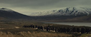 Movie still from “Macbeth” (2015), directed by Justin Kurzel – A large group of people walking on a path in the mountains; Extreme Wide shot, High angle
