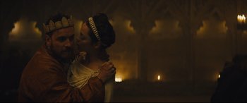 Movie still from “Macbeth” (2015), directed by Justin Kurzel – A man and a woman embracing each other in front of candles; Medium shot, Low angle