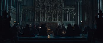 Movie still from “Macbeth” (2015), directed by Justin Kurzel – A group of people sitting in a dark room; Wide shot, Low angle