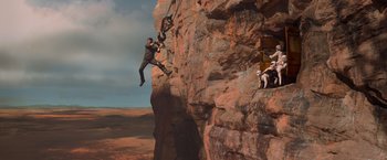 Movie still from “Mad Max: Fury Road” (2015), directed by George Miller – A man on a rope is climbing up a rock wall; Wide shot, Low angle