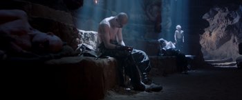 Movie still from “Mad Max: Fury Road” (2015), directed by George Miller – A man sitting on top of a rock in a room; Wide shot, Low angle