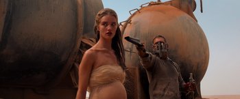 Movie still from “Mad Max: Fury Road” (2015), directed by George Miller – A woman standing next to a man holding a remote control; Medium shot, Over the shoulder angle