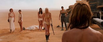 Movie still from “Mad Max: Fury Road” (2015), directed by George Miller – A group of women standing in the desert with a gun; Wide shot, Over the shoulder angle