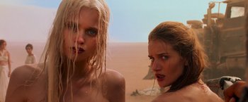 Movie still from “Mad Max: Fury Road” (2015), directed by George Miller – Two beautiful young women standing next to each other on the beach; Close Up shot, Low angle