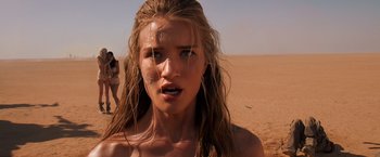 Movie still from “Mad Max: Fury Road” (2015), directed by George Miller – A woman with long blonde hair standing in the desert; Close Up shot, Over the shoulder angle