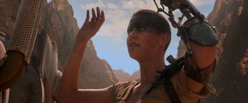 Movie still from “Mad Max: Fury Road” (2015), directed by George Miller – A woman with a shaved head is holding her hand up to the sky; Close Up shot, Low angle