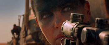 Movie still from “Mad Max: Fury Road” (2015), directed by George Miller – A person with a gun looking through a scope; Close Up shot, Over the shoulder angle