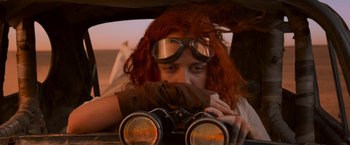 Movie still from “Mad Max: Fury Road” (2015), directed by George Miller – A woman with red curly hair wearing goggles looking through a pair of binoculars; Close Up shot, Low angle