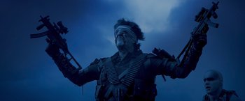 Movie still from “Mad Max: Fury Road” (2015), directed by George Miller – A man with a blindfold on is holding a gun; Medium shot, Low angle