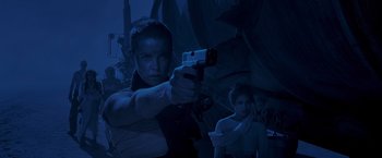 Movie still from “Mad Max: Fury Road” (2015), directed by George Miller – A man holding a gun while standing next to a woman; Medium shot, Low angle