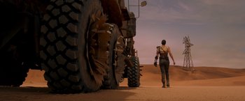 Movie still from “Mad Max: Fury Road” (2015), directed by George Miller – A man walking next to a large truck; Wide shot, Low angle