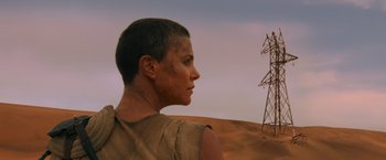 Movie still from “Mad Max: Fury Road” (2015), directed by George Miller – A man standing next to a power pole in the desert; Medium shot, Low angle