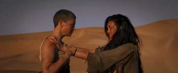 Movie still from “Mad Max: Fury Road” (2015), directed by George Miller – A man and a woman in the desert touching each other; Medium shot, Over the shoulder angle