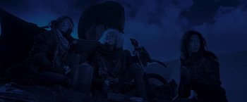 Movie still from “Mad Max: Fury Road” (2015), directed by George Miller – A man sitting on top of a chair under an umbrella at night; Wide shot, Low angle