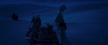 Movie still from “Mad Max: Fury Road” (2015), directed by George Miller – Two people standing next to a motorcycle in the dark; Wide shot, Low angle