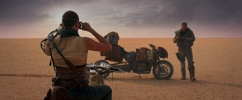 Movie still from “Mad Max: Fury Road” (2015), directed by George Miller – A man sitting on the back of a motorcycle in the desert; Wide shot, Over the shoulder angle