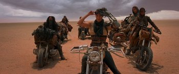 Movie still from “Mad Max: Fury Road” (2015), directed by George Miller – A woman sitting on the back of a motorcycle in the middle of the desert; Wide shot, Low angle