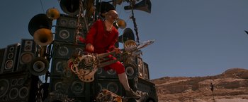 Movie still from “Mad Max: Fury Road” (2015), directed by George Miller – A man in a red outfit is playing a guitar; Wide shot, Low angle