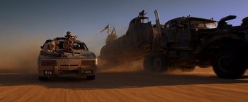 Movie still from “Mad Max: Fury Road” (2015), directed by George Miller – A truck driving down a dirt road next to a train; Wide shot, Low angle