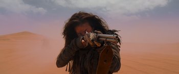 Movie still from “Mad Max: Fury Road” (2015), directed by George Miller – A woman with long hair is holding a gun; Medium shot, Over the shoulder angle