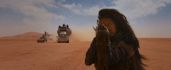 Movie still from “Mad Max: Fury Road” (2015), directed by George Miller – A woman holding a gun while standing in front of a truck; Medium shot, Over the shoulder angle