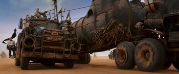 Movie still from “Mad Max: Fury Road” (2015), directed by George Miller – A truck driving down a dirt road next to an airplane; Wide shot, Low angle