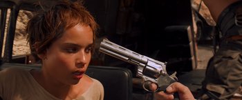Movie still from “Mad Max: Fury Road” (2015), directed by George Miller – A young girl holding a gun up to her face; Close Up shot, Over the shoulder angle