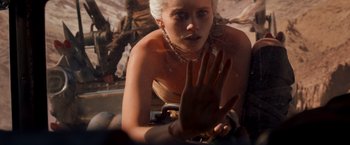 Movie still from “Mad Max: Fury Road” (2015), directed by George Miller – A woman with white hair is sitting on a skateboard; Close Up shot, Over the shoulder angle