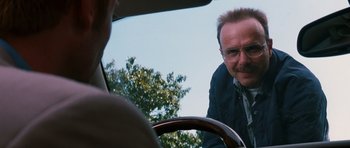 Movie still from “Memento” (2000), directed by Christopher Nolan – A man with glasses is sitting in the driver's seat of a car; Close Up shot, Over the shoulder angle