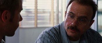 Movie still from “Memento” (2000), directed by Christopher Nolan – A person with a mustache wearing glasses; Close Up shot, Over the shoulder angle