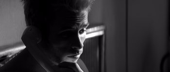 Movie still from “Memento” (2000), directed by Christopher Nolan – Black and white photograph of a young man with his hand on his chin; Close Up shot, Low angle