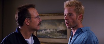 Movie still from “Memento” (2000), directed by Christopher Nolan – A man and a man in a room with a painting on the wall behind them; Close Up shot, Over the shoulder angle