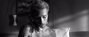 Movie still from “Memento” (2000), directed by Christopher Nolan – A shirtless man with a tie is talking on a phone; Close Up shot, Low angle