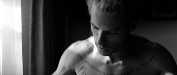 Movie still from “Memento” (2000), directed by Christopher Nolan – A person with tattoos on their chest; Close Up shot, Low angle