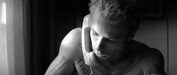 Movie still from “Memento” (2000), directed by Christopher Nolan – A man with tattoos on his arms and head is holding a phone; Close Up shot, Overhead angle