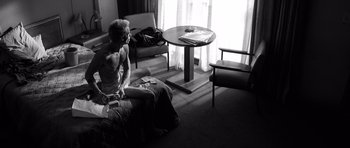 Movie still from “Memento” (2000), directed by Christopher Nolan – A woman sitting on a bed in a room; Wide shot, High angle