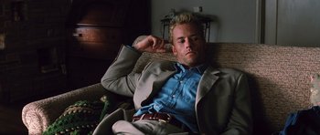Movie still from “Memento” (2000), directed by Christopher Nolan – A man sitting on a couch wearing a suit and tie; Medium shot, Low angle