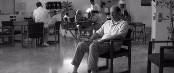 Movie still from “Memento” (2000), directed by Christopher Nolan – A group of people sitting in chairs in a room; Wide shot, Over the shoulder angle