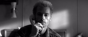 Movie still from “Memento” (2000), directed by Christopher Nolan – A black and white photo of a man holding a phone to his ear; Close Up shot, Low angle