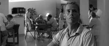 Movie still from “Memento” (2000), directed by Christopher Nolan – A black - and - white photo of a man in front of a group of people; Close Up shot, Low angle