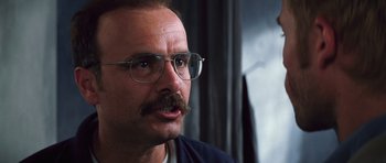 Movie still from “Memento” (2000), directed by Christopher Nolan – A person with a mustache wearing glasses; Close Up shot, Low angle