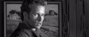 Movie still from “Memento” (2000), directed by Christopher Nolan – Black and white photograph of a man in front of a painting; Close Up shot, Over the shoulder angle