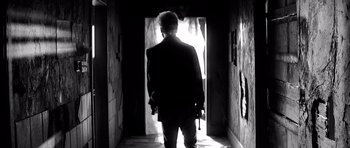 Movie still from “Memento” (2000), directed by Christopher Nolan – A man walking down a hall way holding a knife; Wide shot, Low angle