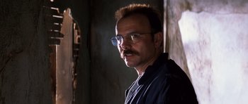 Movie still from “Memento” (2000), directed by Christopher Nolan – A man with a mustache wearing glasses and a black shirt; Close Up shot, Low angle