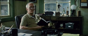 Movie still from “Million Dollar Baby” (2004), directed by Clint Eastwood – An older man sitting at a desk reading a book; Medium shot, Low angle