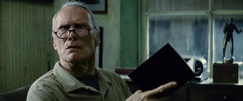 Movie still from “Million Dollar Baby” (2004), directed by Clint Eastwood – An older man sitting in a chair holding a book; Close Up shot, Low angle